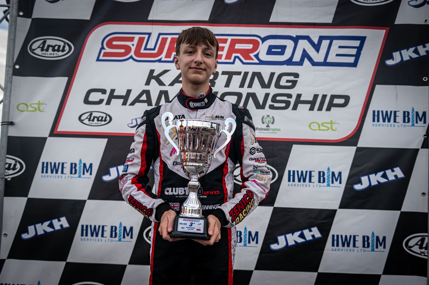 Zak Jennings in Zenico Racing overalls holding his third-place trophy on the Super One podium